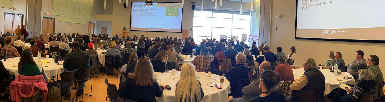 view of Student Union Ballroom filled with round tables and people listening to presentation at the front of the room